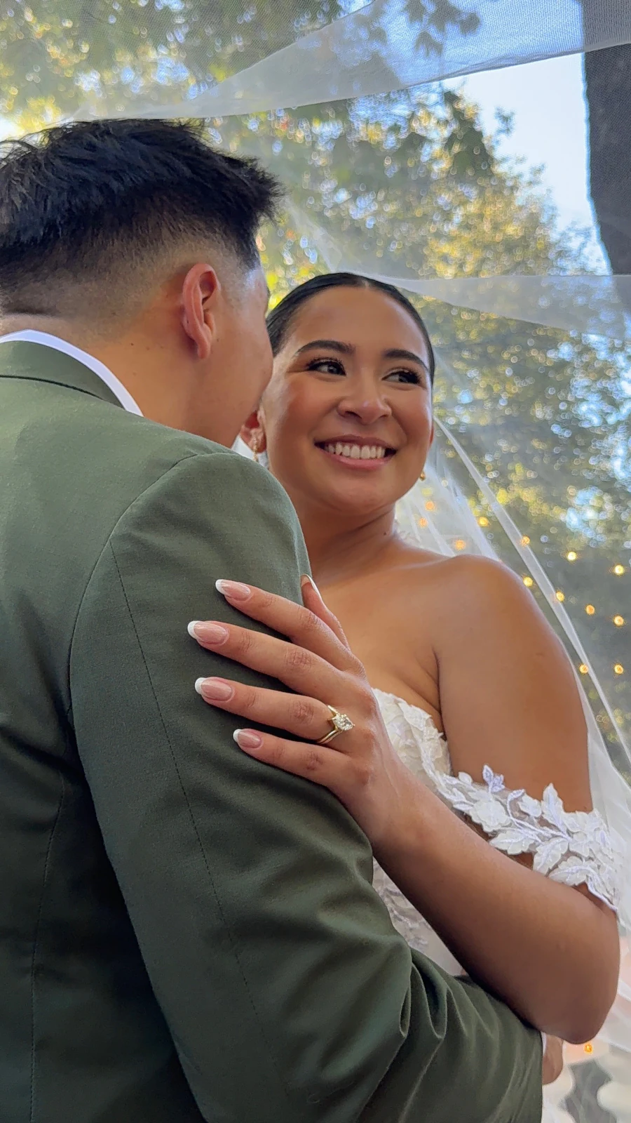 Bride smiling while embracing her partner beneath her veil