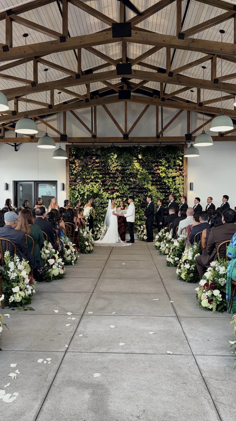 Wedding ceremony inside a timber-beam venue with a living green wall